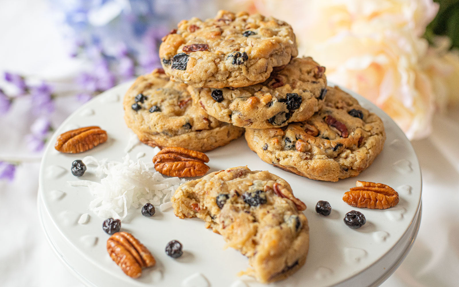 Blueberry coconut pecan cookies arranged on a plate, surrounded by shredded coconut, pecans, and dried blueberries.
