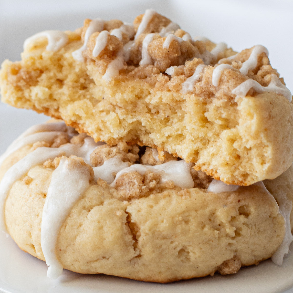 Overhead view of a Crumb Cake Cookie with a crumbly streusel topping and a vanilla glaze drizzle on a white plate.
