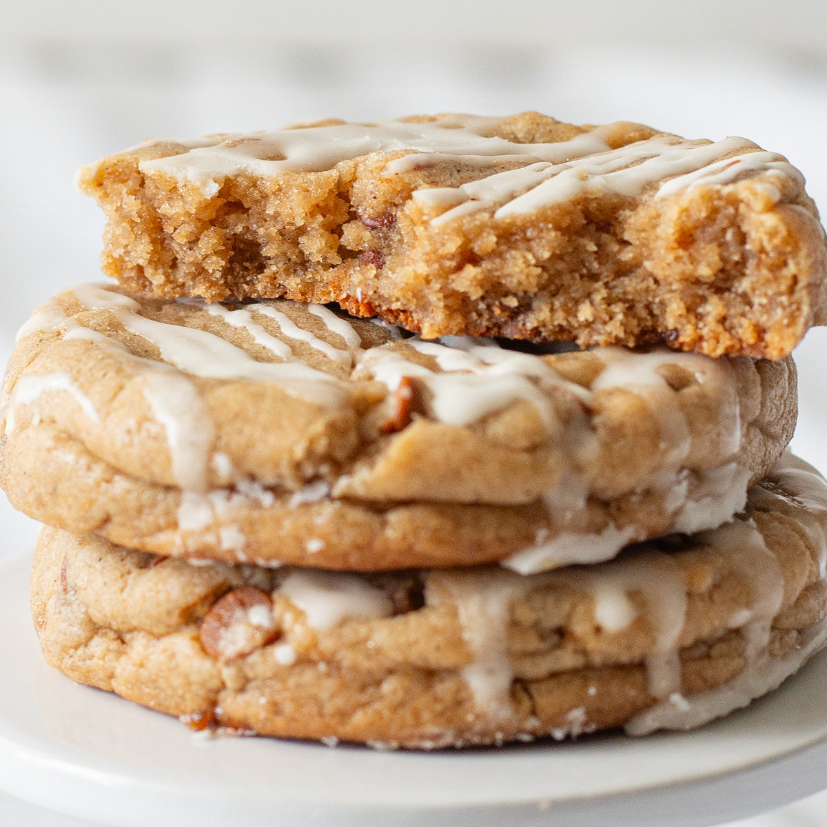 Stack of three Apple Cider Cookies, with the top one split in half to reveal a soft, cinnamon-speckled inside. The cookies are topped with a glossy apple cider glaze, adding a sweet and autumnal touch.