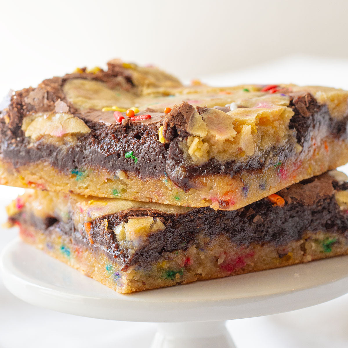 An enticing close-up photo of two layered Birthday Cake Brownies, showcasing the distinct layers of cake-flavored cookie dough and rich chocolate brownie.