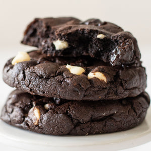 stack of 3 Black Cherry Noir Cookies, one broken in half to show the white chocolate chips and cherry chunks