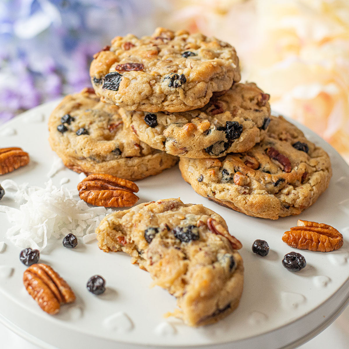 Blueberry coconut pecan cookies arranged on a plate, surrounded by shredded coconut, pecans, and dried blueberries.