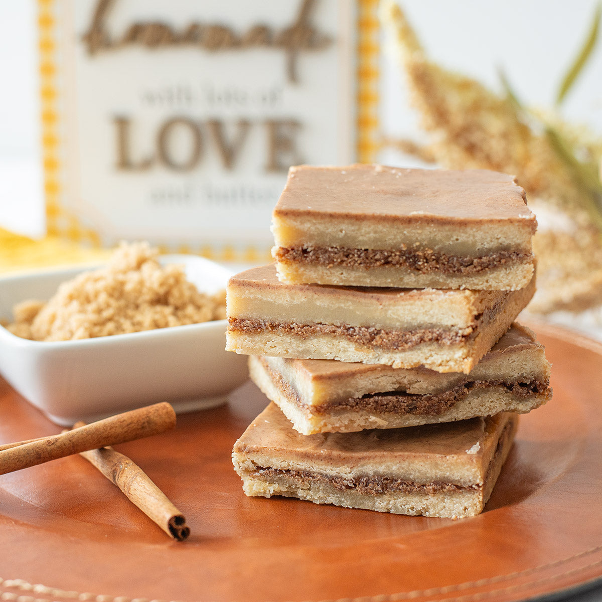 A stack of Brown Sugar & Spice Delight Bars on a plate, paired with a dish of brown sugar and cinnamon sticks—everything you need for a sweet, spiced treat.