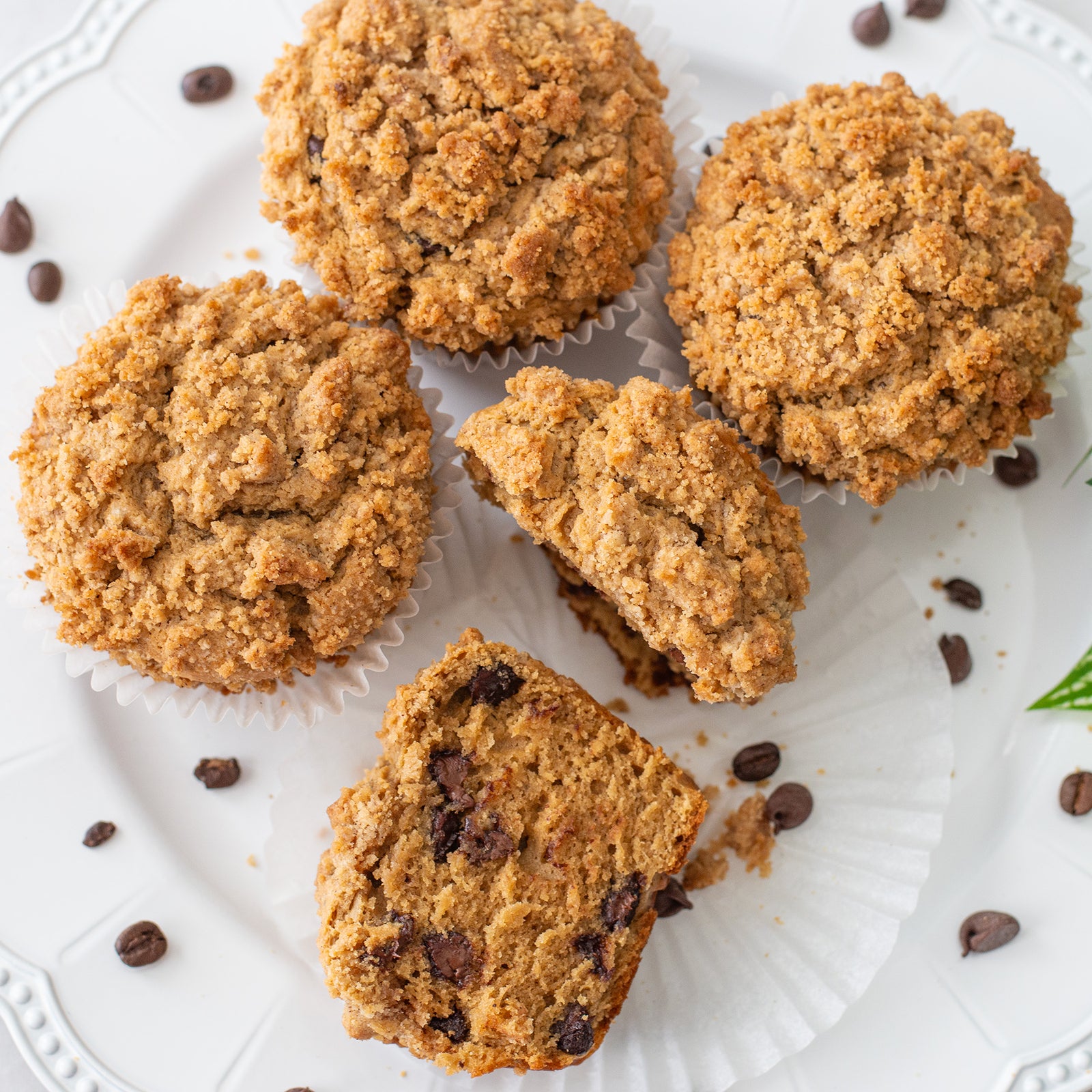 Single cappuccino muffin on a pedestal stand, topped with a golden-brown cinnamon streusel and visible chocolate chips, set against a softly lit background.