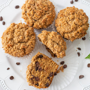 Five chocolate chip muffins on a white plate with scattered chocolate chips and coffee beans.