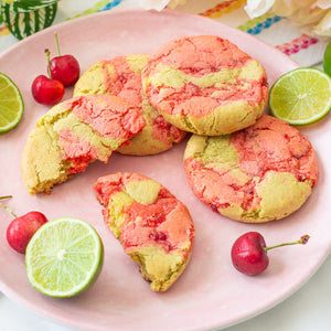 Cherry Limeade Cookies on a plate, surrounded by fresh lime slices and sweet red cherries.