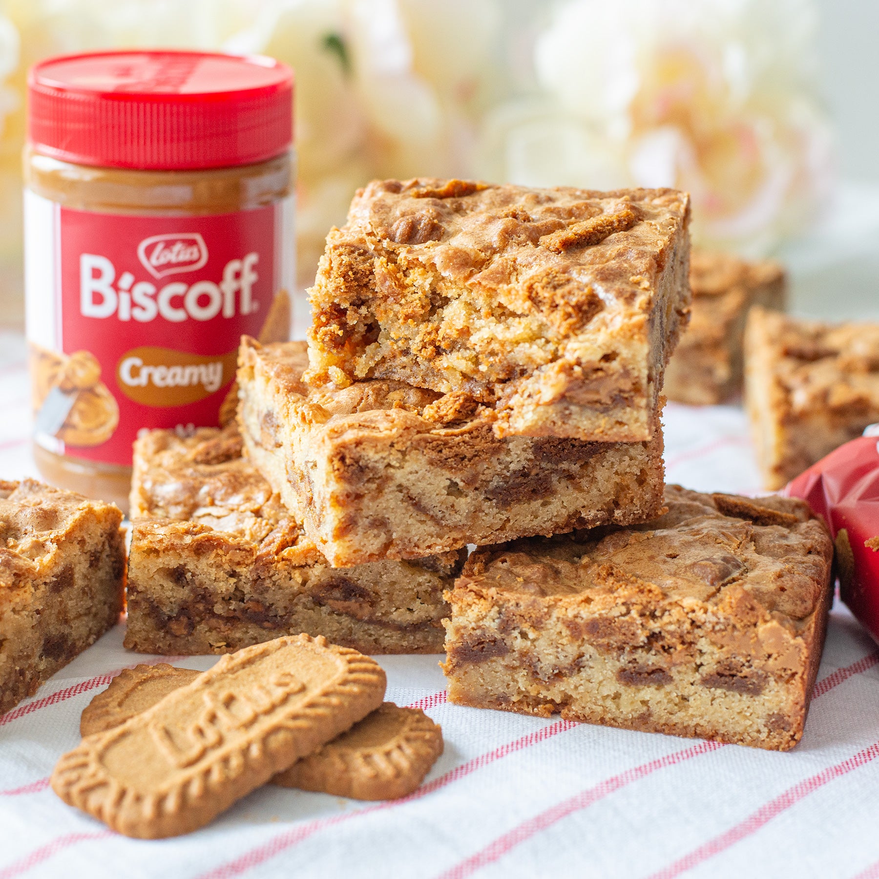 Cookie Butter Blondies with a jar of Biscoff spread on a tablecloth, with Biscoff cookies in front.