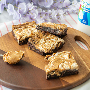 A delicious looking image of Fluffernutter Brownies on a plate with a spoon of peanut butter and marshmallow creme in the background.