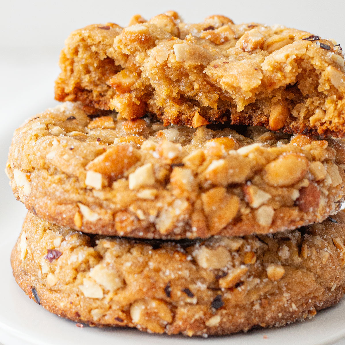 A mouthwatering image of a Hot-Honey Peanut Butter Cookie, showcasing its golden-brown exterior, chunky texture from the chopped honey-roasted peanuts, and a sprinkle of chili pepper flakes for a touch of heat.