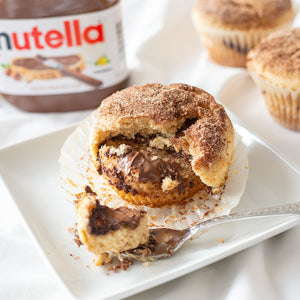 A close-up photo of a freshly baked Nutella Muffin, highlighting its moist texture and gooey Nutella filling, encapsulated by a cinnamon-sugar coating, offering a delightful combination of flavors.