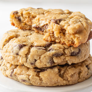 Stack of Oatmeal Choco-Peanut Butter Delight Cookies on a white plate, with one broke open to show the melty chocolate and peanut butter chips.