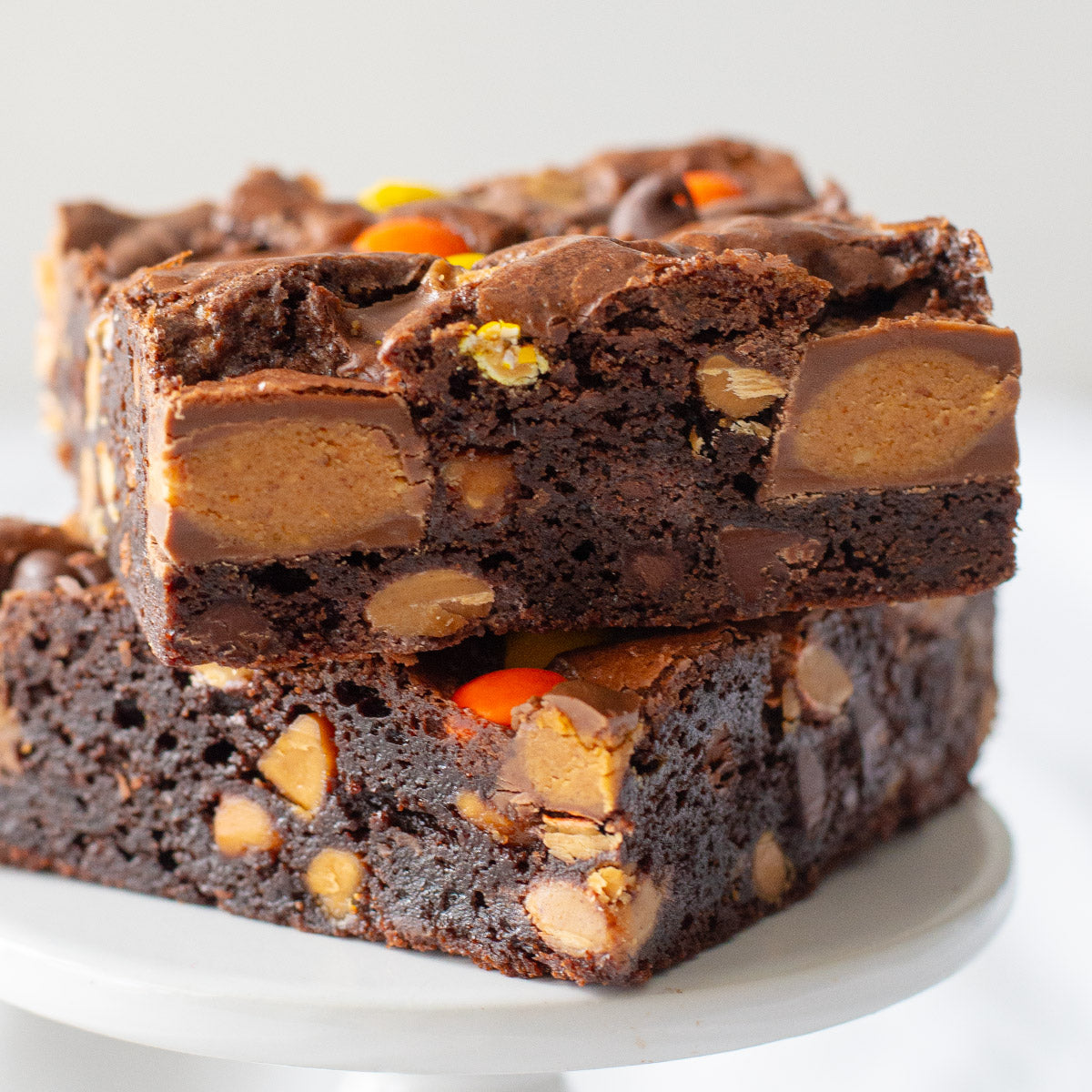 A tantalizing view from above showcasing a delectable P.B. Party Brownie, featuring a rich, fudgy base studded with peanut butter cups and chocolate peanut butter chips, topped with a generous sprinkle of chopped peanut butter cups and chocolate peanut butter candies, promising a mouthwatering blend of flavors in every bite.