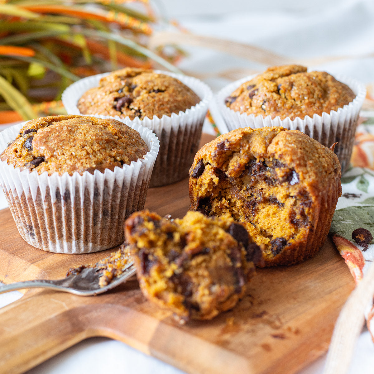 A single Pumpkin Chocolate Chip Muffin sits upright, its top domed and slightly cracked, revealing chunks of semi-sweet and milk chocolate chips. The warm orange hue of the pumpkin contrasts with the speckled chocolate, making it look moist and freshly baked.