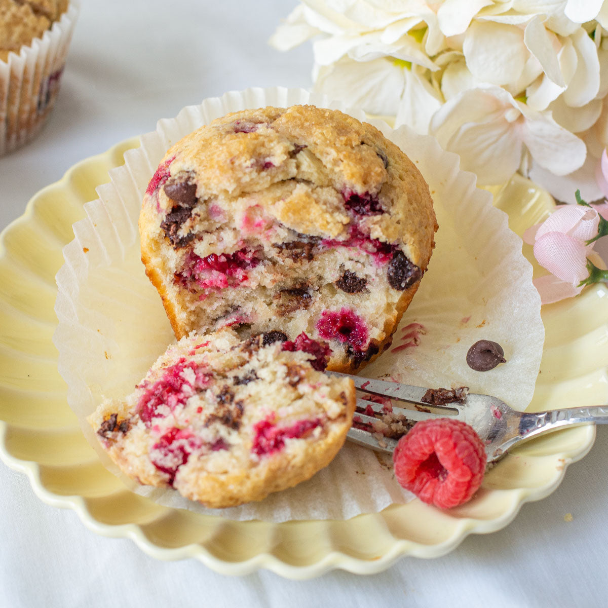 A close-up image of a Jumbo Raspberry Chocolate Chip Muffin with visible chunks of raspberries and chocolate chips on top.