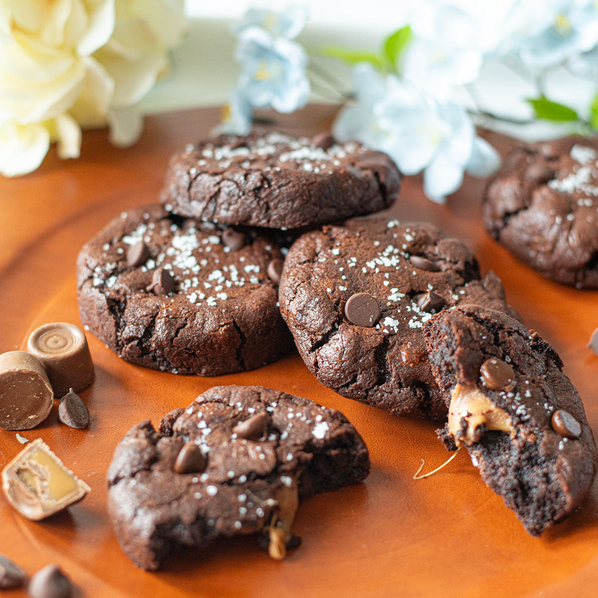 An assortment of tempting Salted Caramel Cookies, capturing the essence of their exquisite flavors by featuring a caramel-filled candy tucked within chocolate cookie dough, complemented by a sprinkle of fleur de sel for an indulgent treat.