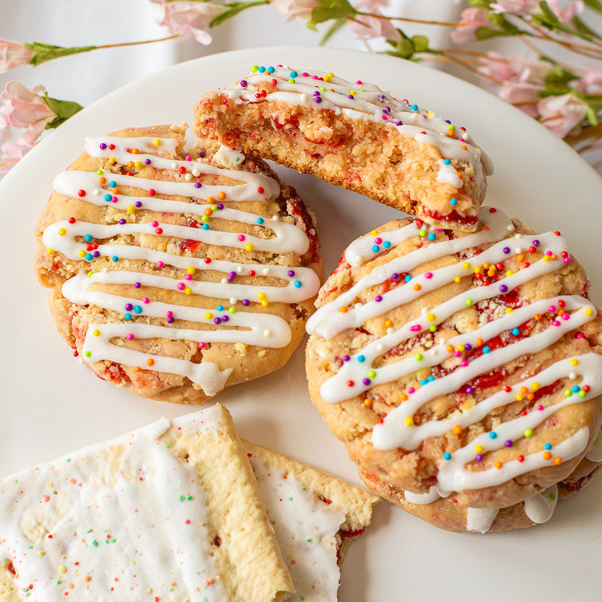 Three Strawberry Pop Tart Cookies arranged on a plate alongside two Strawberry Pop Tarts, showcasing their resemblance and deliciousness.