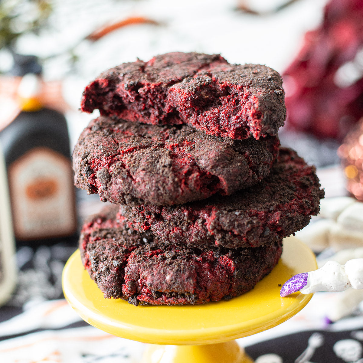 A stack of Velvet Vortex Cookies with their dark Oreo crust and red velvet centers, set against a spooky backdrop featuring eerie Halloween decorations.