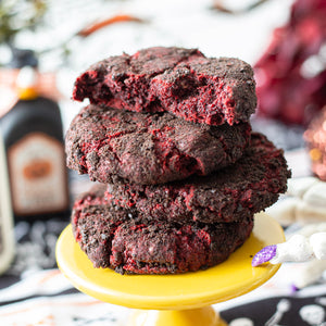 A stack of Velvet Vortex Cookies with their dark Oreo crust and red velvet centers, set against a spooky backdrop featuring eerie Halloween decorations.